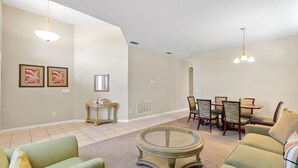 A living room with a round coffee table, green sofas, a dining table with chairs, and pendant lighting.