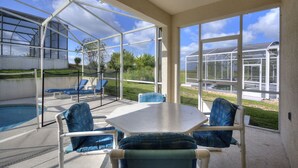 A covered patio with a pool, blue cushioned chairs, and a table.