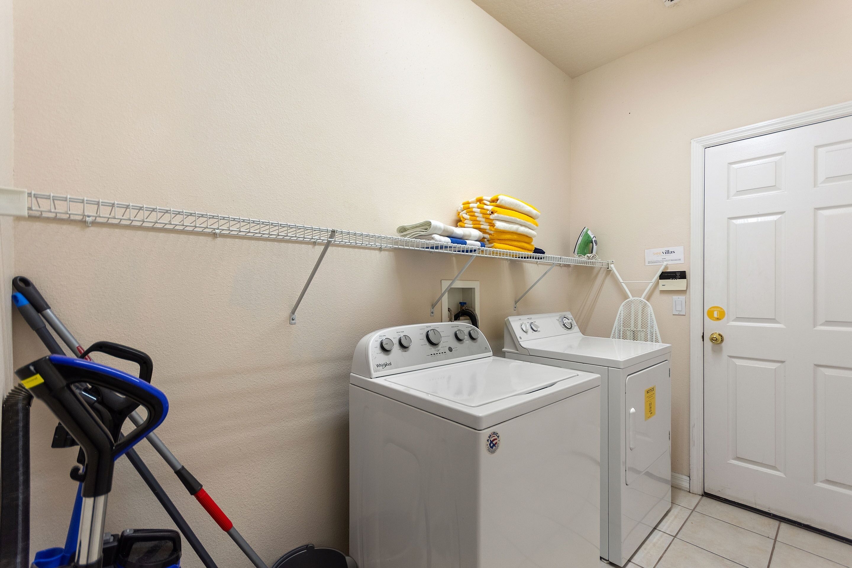 A laundry room with two front-loading washers and dryers, a metal drying rack, and a vacuum cleaner.