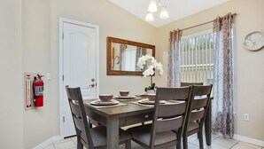 A dining area with a wooden table set for four, a fire extinguisher on the wall, a mirror above the table, and a window with curtains. - Tranquil Hideaway At Sandy Ridge 4 Bedroom Home (Davenport)