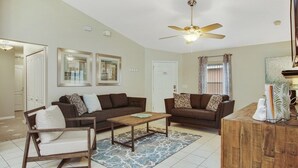A living room with two sofas, a coffee table, a chair, a ceiling fan, and a door. - Tranquil Hideaway At Sandy Ridge 4 Bedroom Home (Davenport)