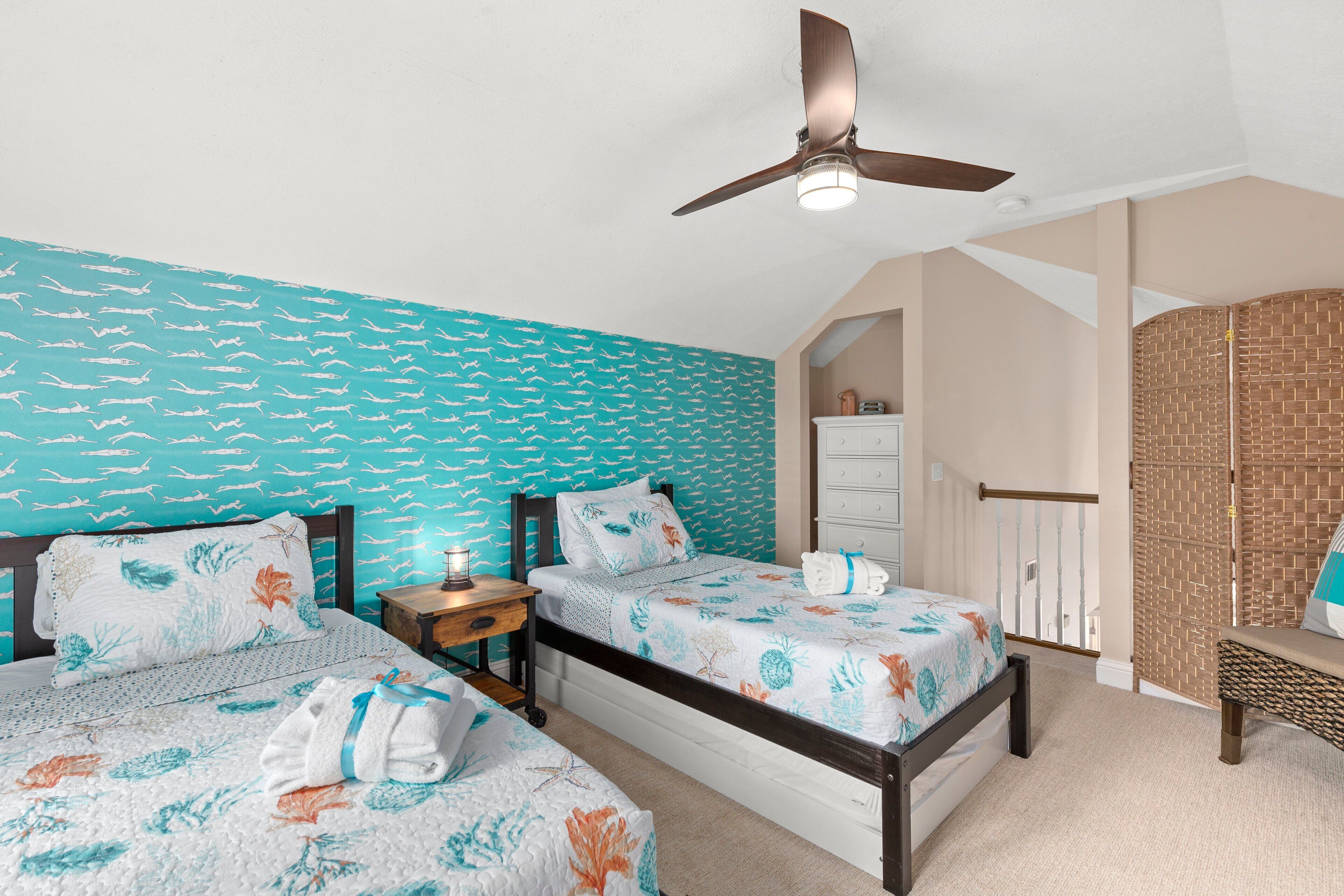Quarto com duas camas, um ventilador de teto e parede com padrão de tijolos.