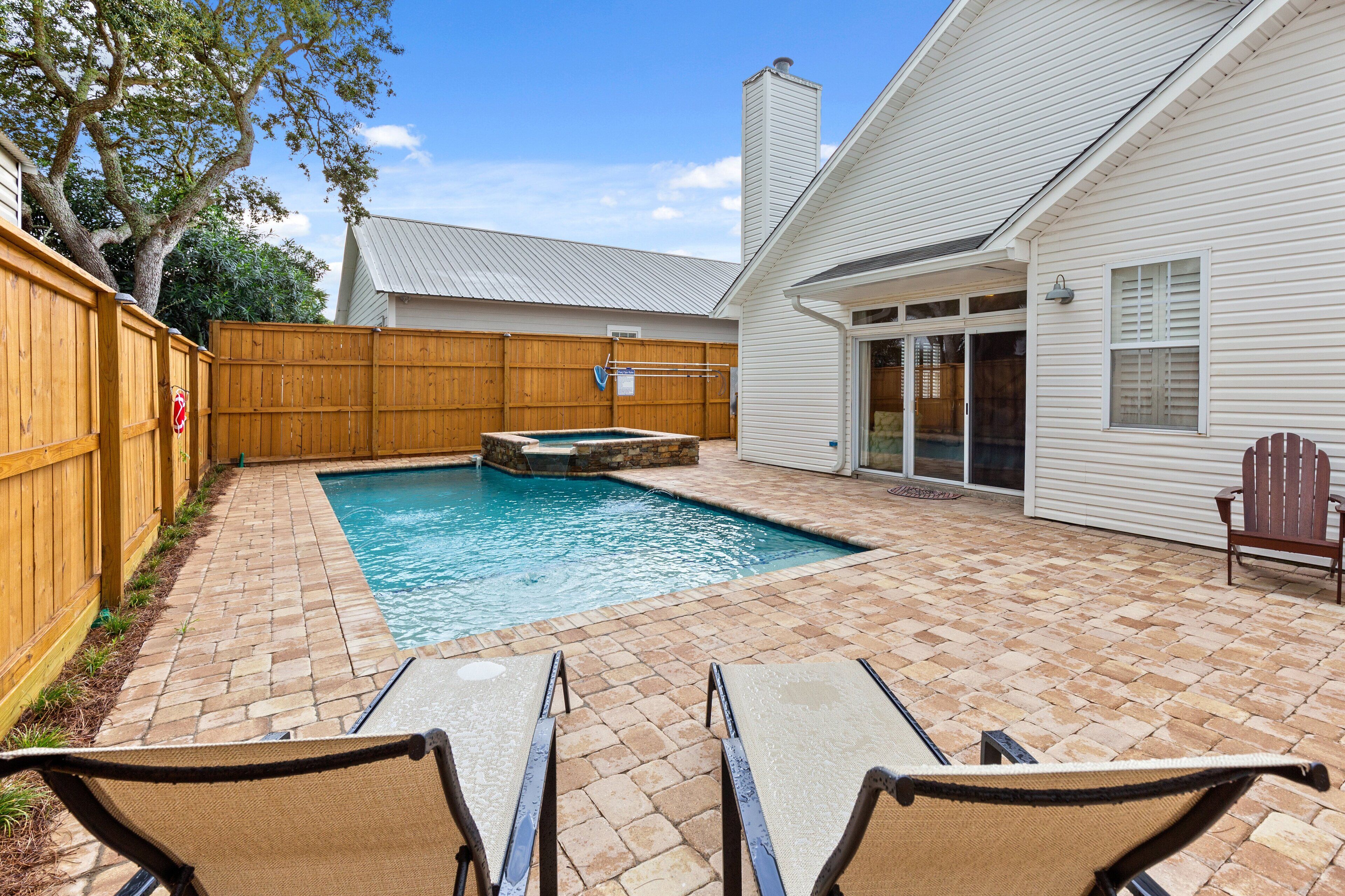 A backyard with a swimming pool, a hot tub, and two lounge chairs.