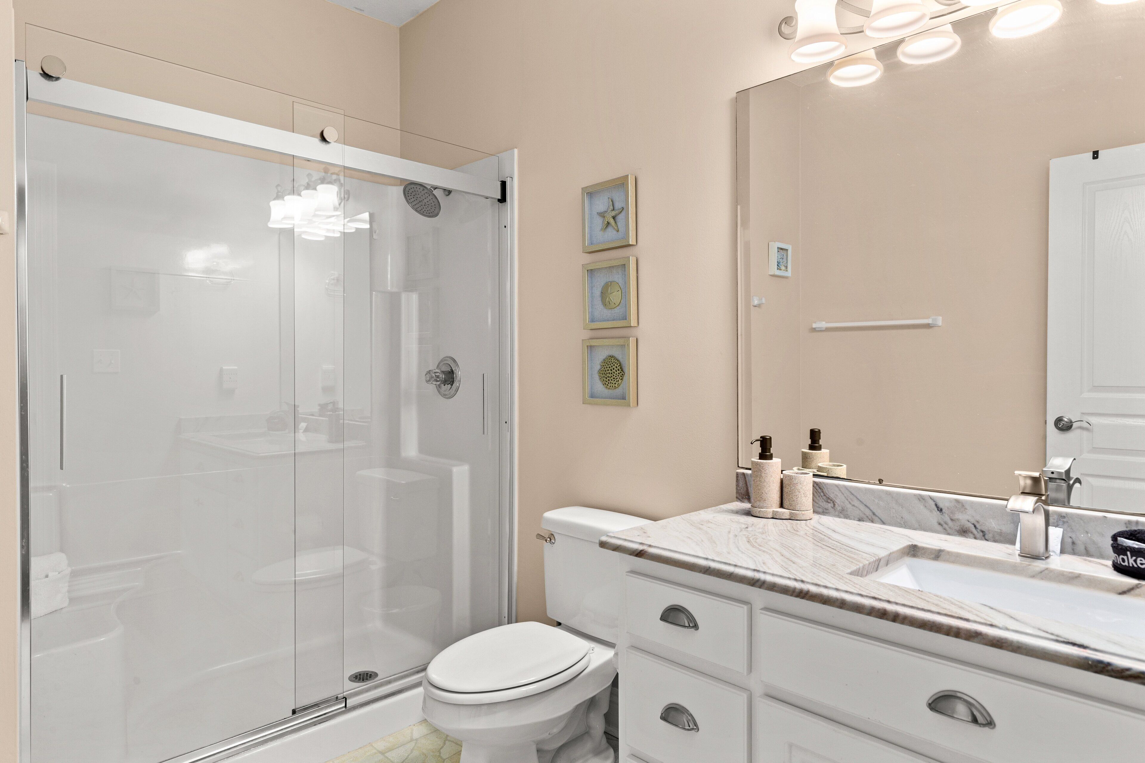 A modern bathroom with a glass-enclosed shower, a white toilet, a marble sink, and a large mirror.