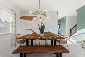 A dining area with a wooden table, chairs, a central plant, and a unique chandelier.