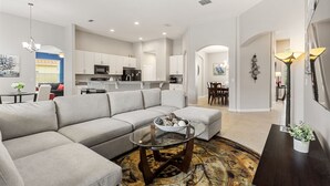 Una sala de estar moderna con un sofá modular, una mesa de centro de vidrio y un comedor con candelabro.