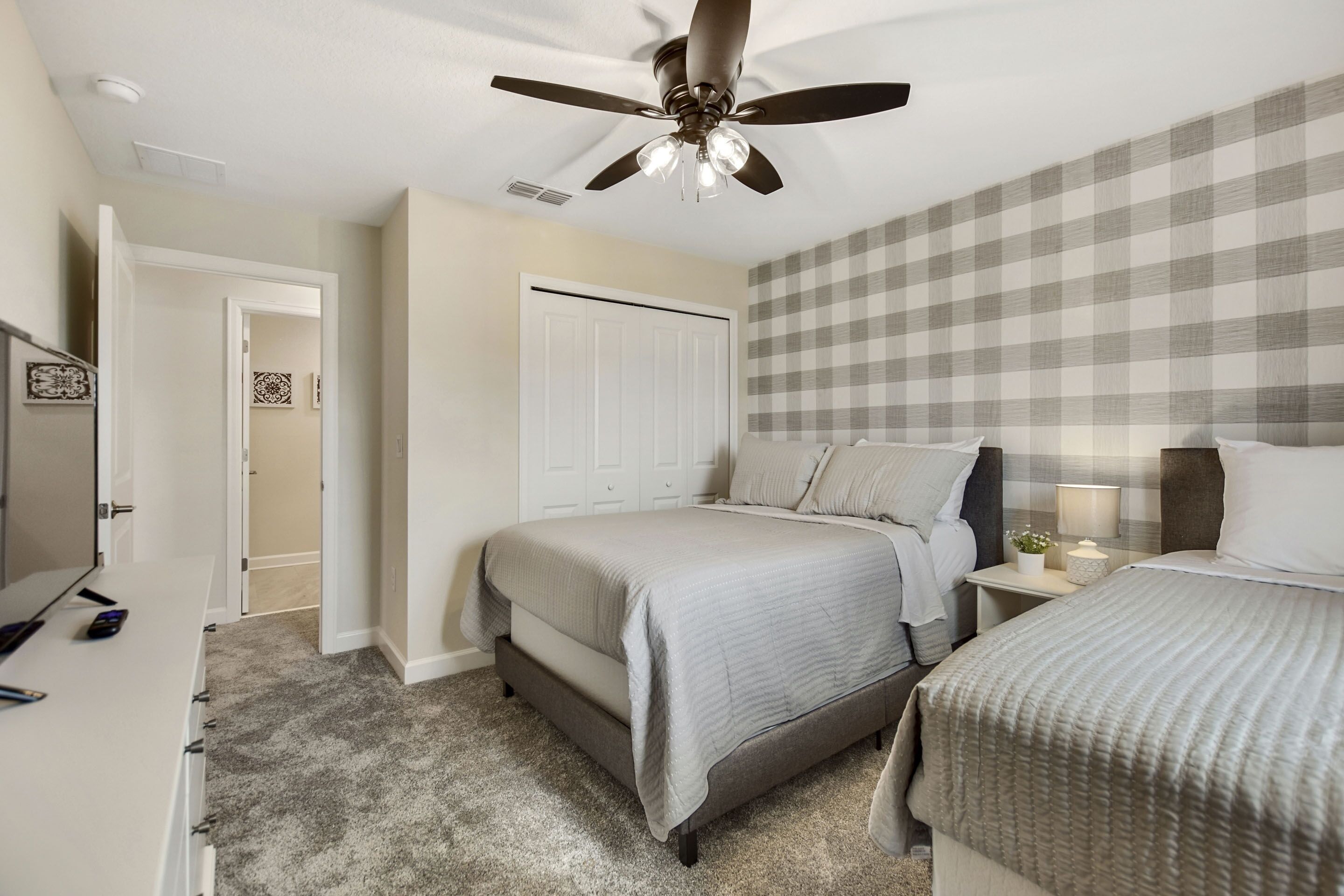 A bedroom with a bed, a nightstand, a ceiling fan, and a door leading to another room.