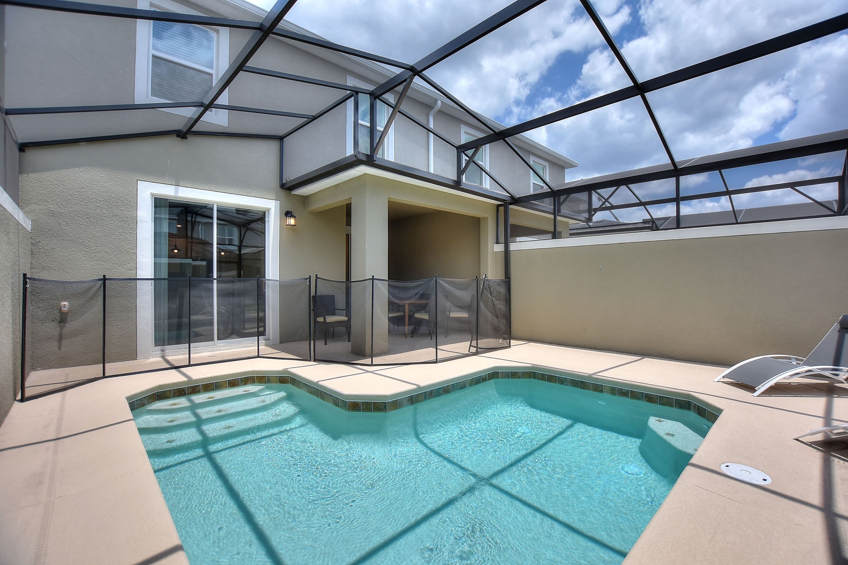 A swimming pool with a glass enclosure, a covered patio area, and a view of the sky.