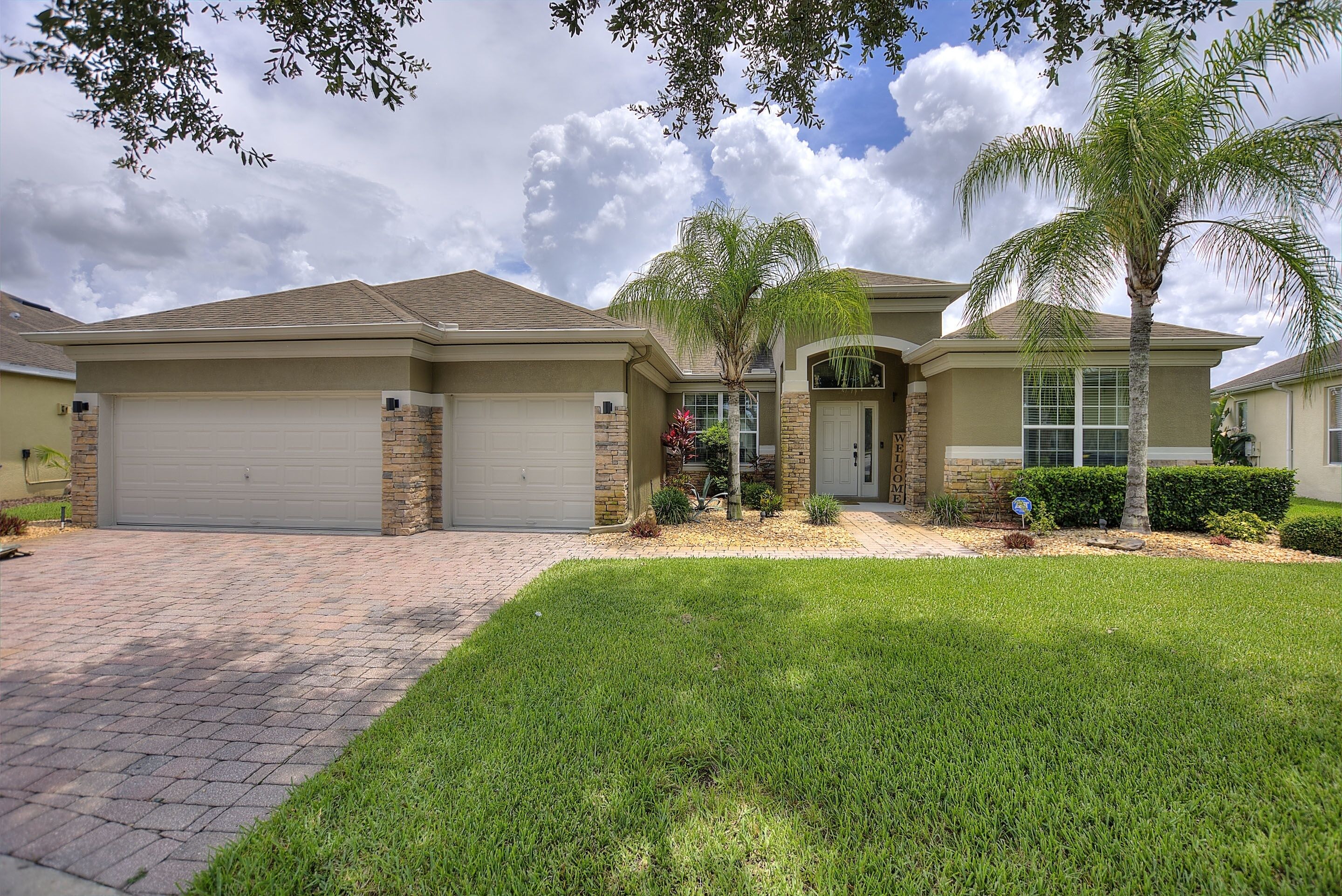 A residential house with a garage, a well-maintained lawn, and a palm tree.
