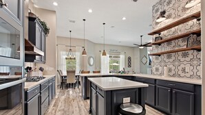 A modern kitchen with dark cabinetry, a central island, and pendant lighting. - Serenity Now By Shine Villas At Watersong #416 5 Bedroom Villa (Davenport)