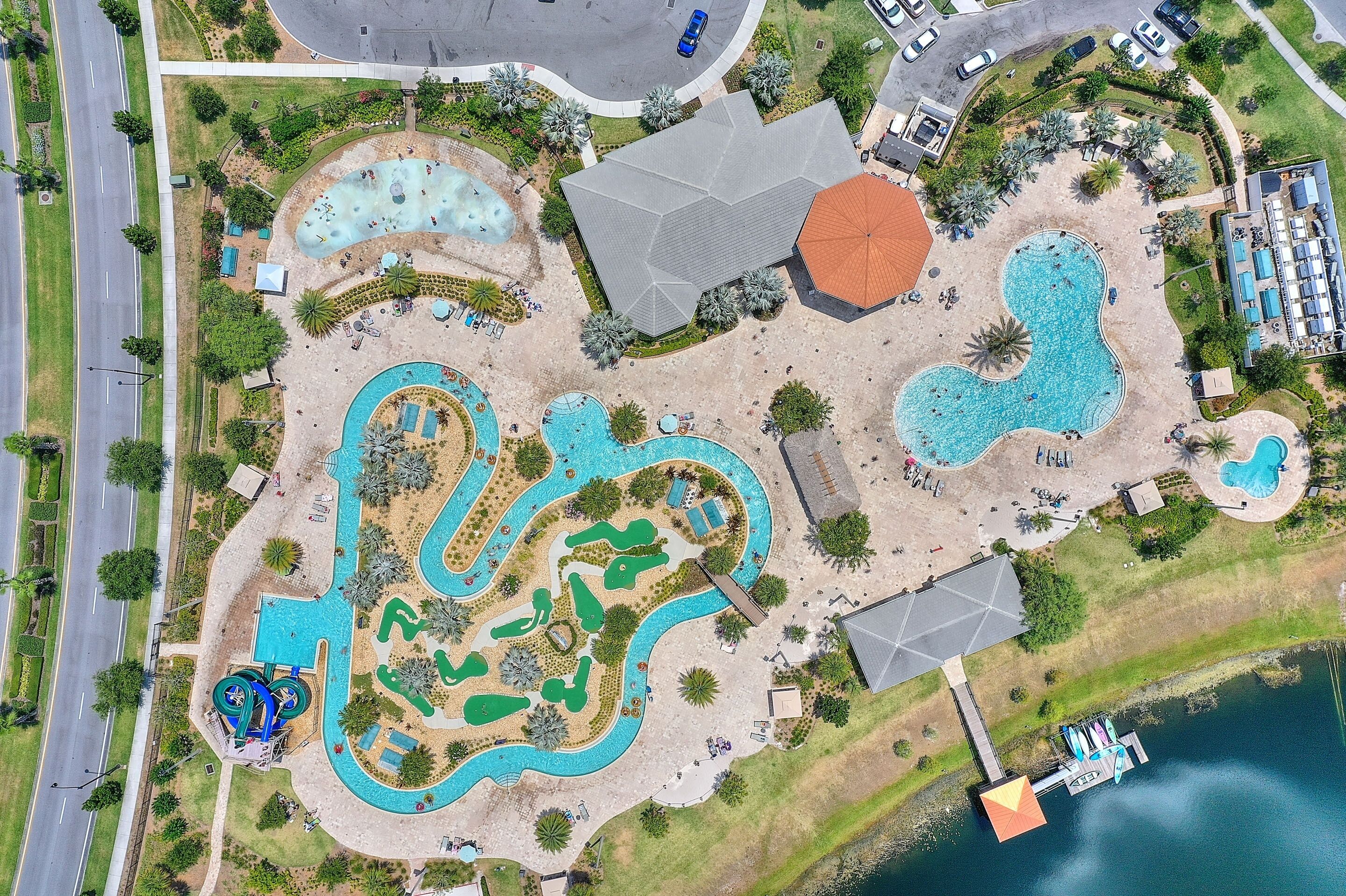 An aerial view of a resort with multiple swimming pools, a large building, and a dock by the water.