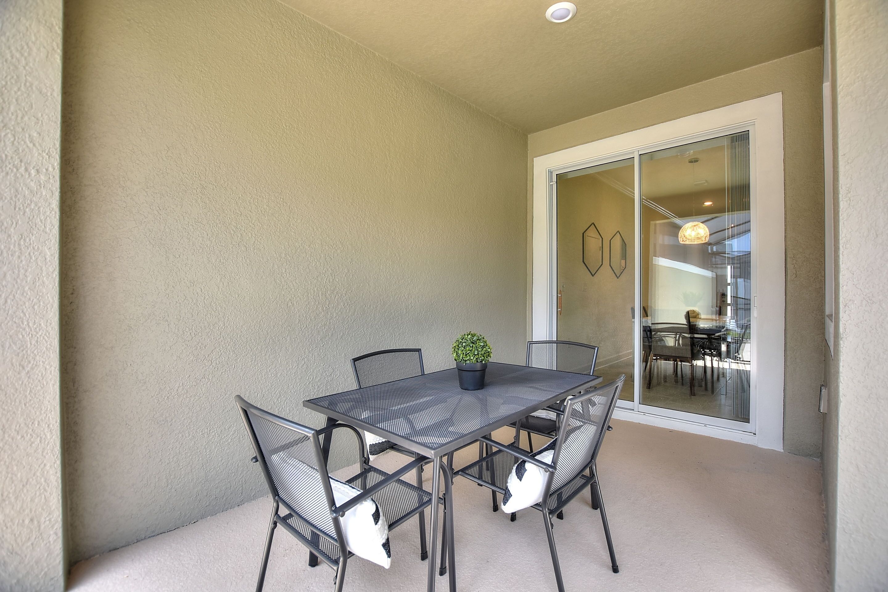 Un balcon avec une table et des chaises, une plante en pot et une porte-fenêtre coulissante donnant sur un espace intérieur comprenant une table et des chaises.