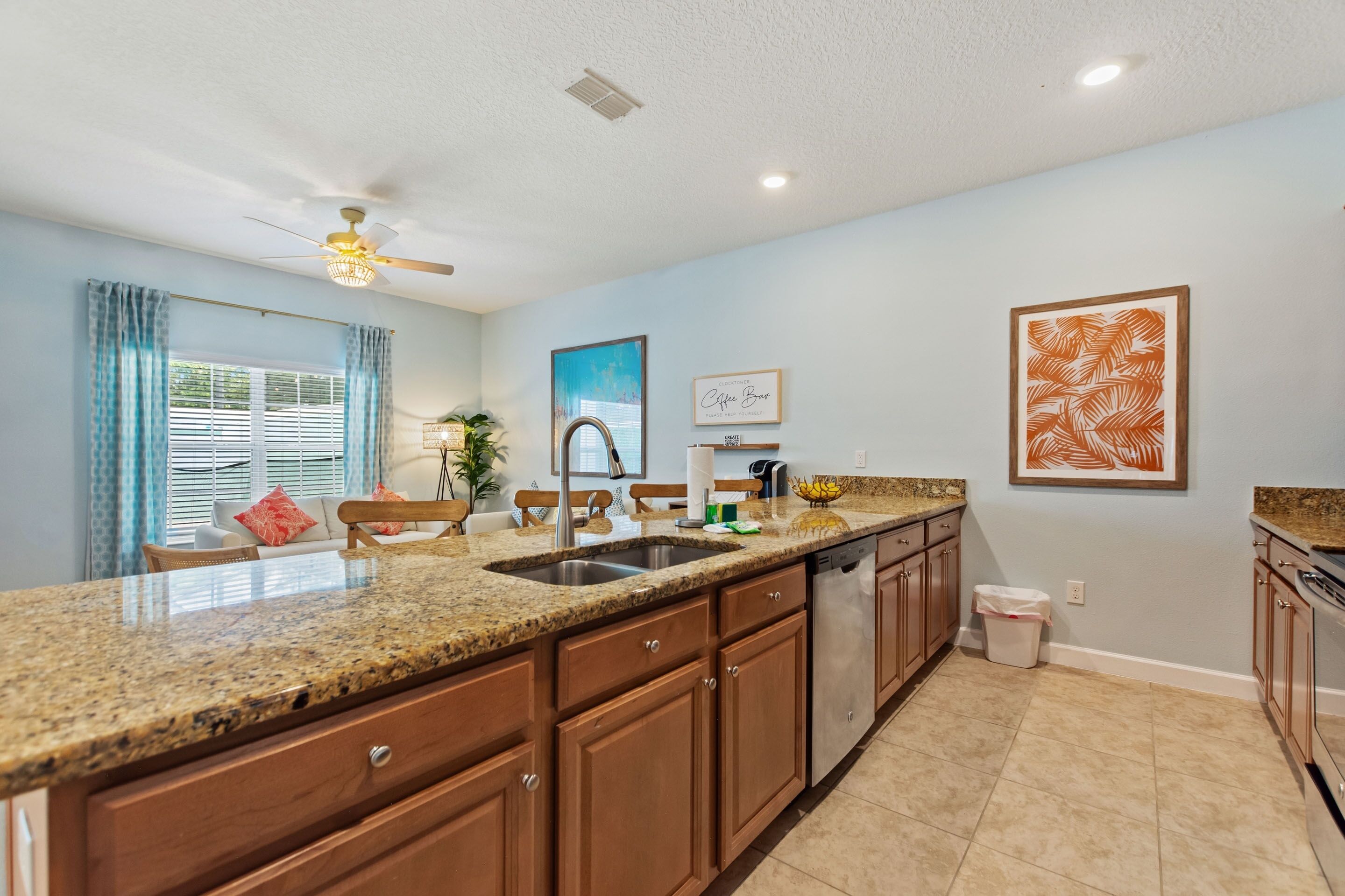 A kitchen with granite countertops, wooden cabinets, a stainless steel sink, and a ceiling fan.