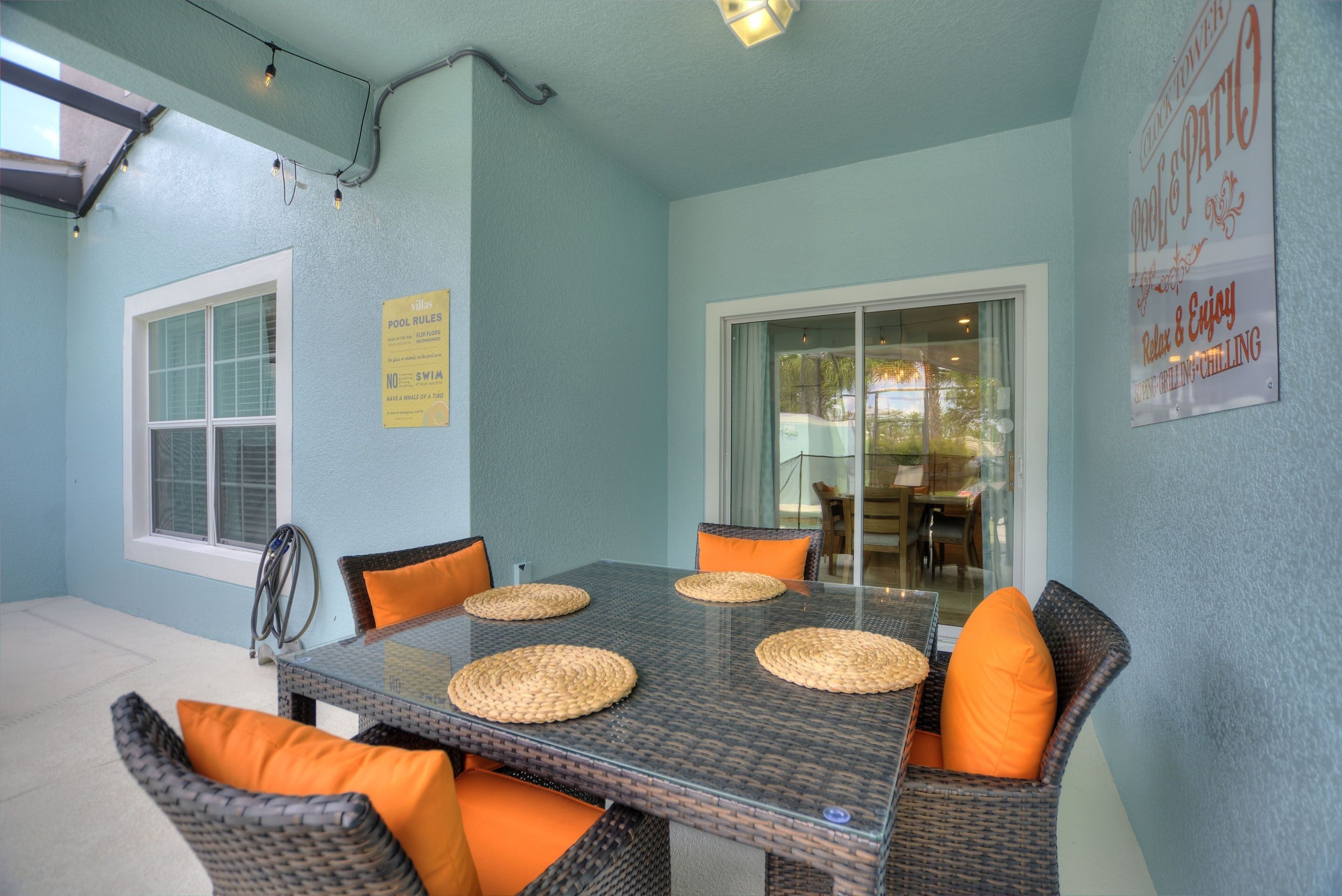 A dining area with a glass table, wicker chairs, and orange cushions.