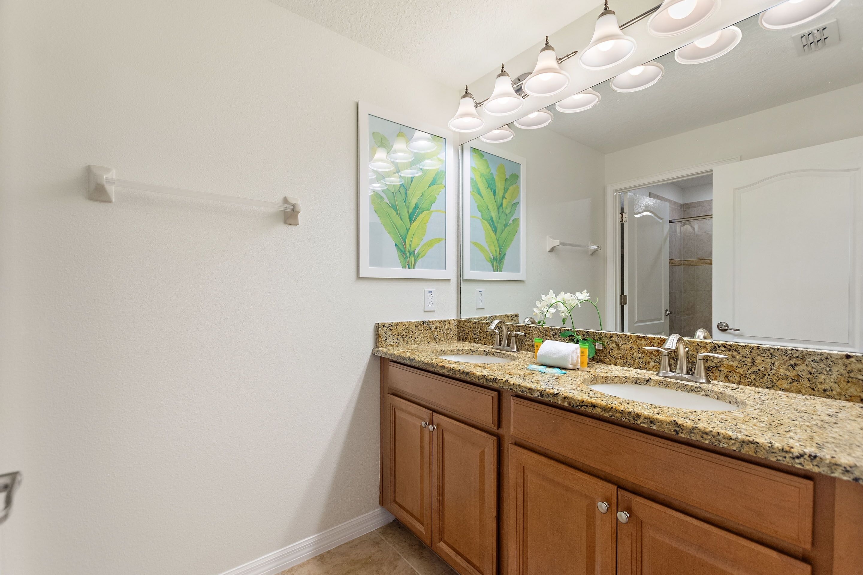 A bathroom with a granite countertop, double sink, wooden cabinets, and a large mirror.