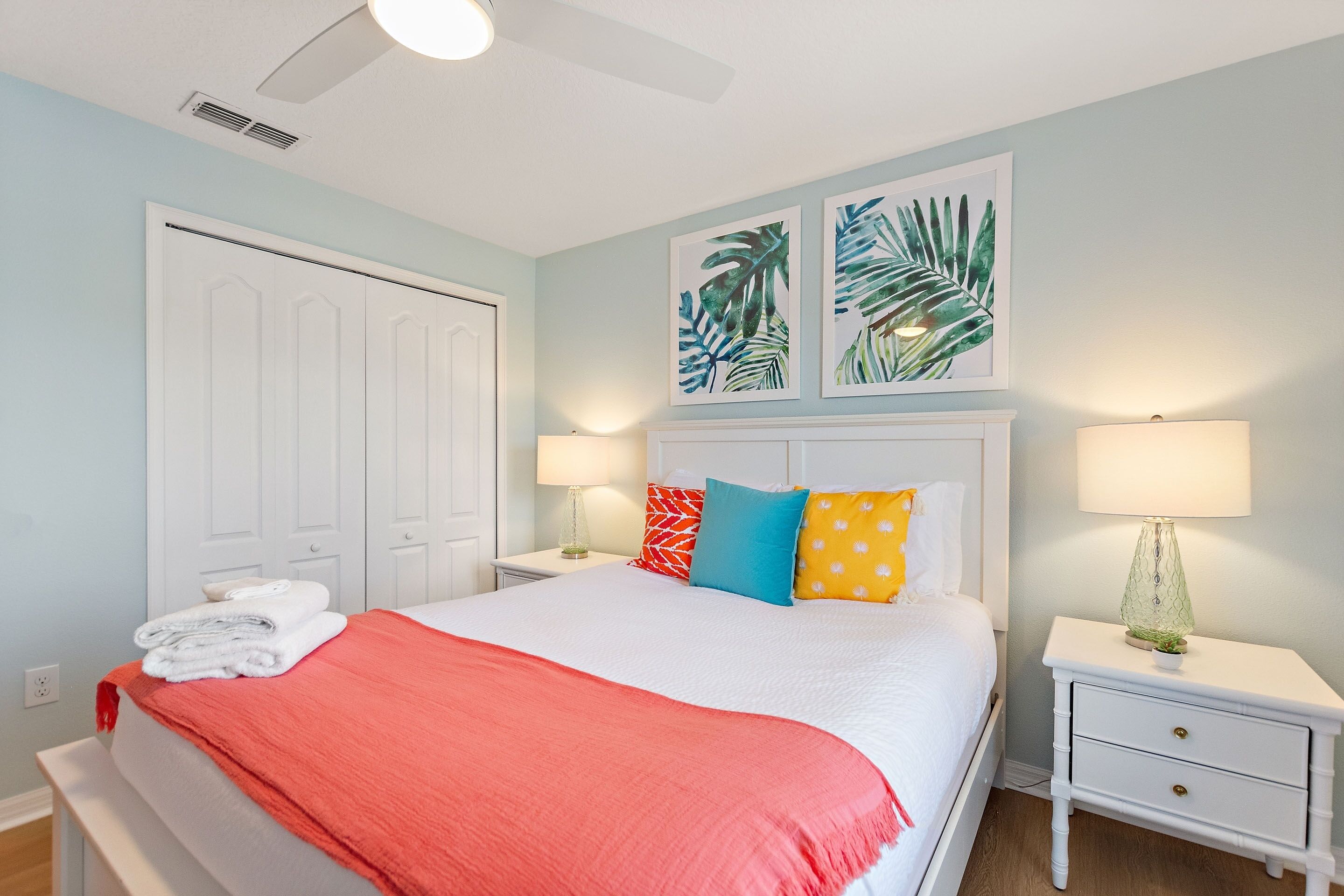 A neatly made bed with a red blanket, white pillows, and a white headboard. There are two bedside tables with lamps and a wall-mounted artwork above the bed.