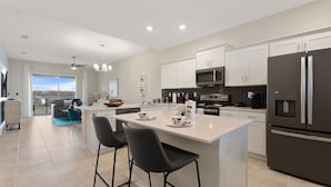 A modern kitchen with white cabinetry, a large island with bar stools, a built-in microwave, and a stainless steel refrigerator. - Edgewater Escape At Storey Lake By Shine Villas 2 Bedroom Apts (Kissimmee)