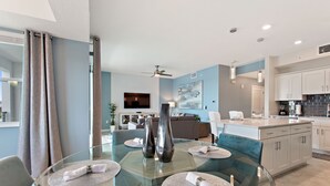 Uma sala de jantar moderna com uma mesa de vidro, dois vasos e um sofá ao fundo.