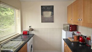 Una cocina con lavadora, un tostador rojo, hervidor y máquina de café.