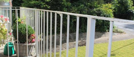 A balcony with white railings overlooking a grassy area and a road.