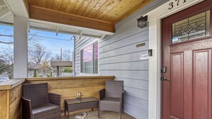 A covered porch with wicker furniture, a wooden table, and a red door. - Newly Built 5bed home 5 min from DT Portland in Laurelhurst Neighborhood (Portland)