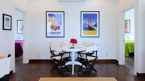 A hotel room with a round dining table, four chairs, and two framed posters on the wall. - Sand Dollar Cottage 2 Bedroom Cottage (Rock Sound)