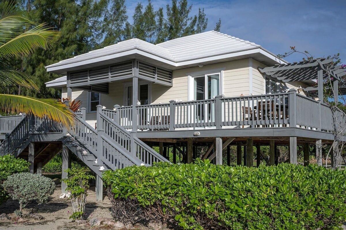 A two-story house with a balcony, a staircase, and a wooden deck. - Sand Dollar Cottage 2 Bedroom Cottage (Rock Sound)