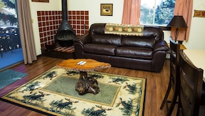 A cozy living room with a leather sofa, a fireplace, a coffee table, and a rug with a forest design. - Elkhorn One Bedroom Condo with River View from Deck and Walking Distance to Estes Park - #3262 by RedAwning (Estes Park)