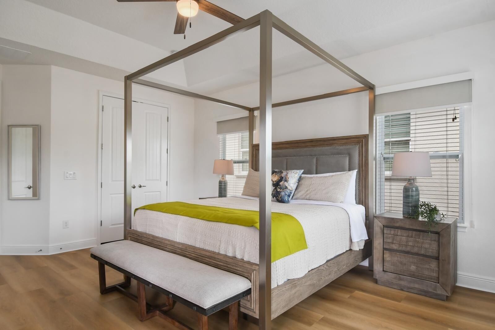 Una cama con dosel, un banco, una mesita de noche con lámpara y una ventana con persianas.