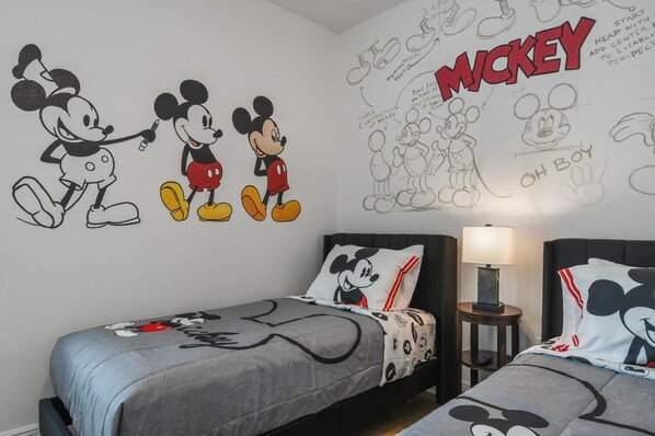 Un dormitorio con dos camas, cada una con ropa de cama temática de Mickey Mouse. Las paredes presentan un gran mural de Mickey Mouse y bocetos de Mickey y Minnie Mouse.