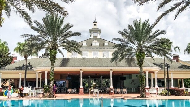 Un hotel con piscina, palmeras y una zona de estar al aire libre techada.