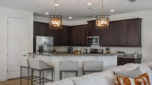 Una cocina moderna con armarios de madera oscura, electrodomésticos de acero inoxidable y dos lámparas colgantes.