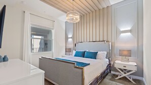 Ein modernes Schlafzimmer mit einem großen Bett, Nachttischen, einer Pendelleuchte und Blick ins Freie.