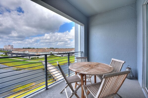 Ein Balkon mit einem runden Holztisch und Stühlen, einem Metallgeländer und Blick auf ein Wohngebiet mit Häusern und einem Grünland.