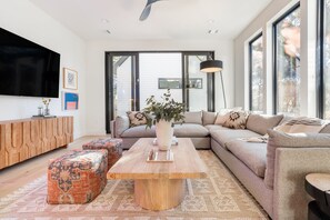 A modern living room with a large sectional sofa, a wooden coffee table, and a flat-screen TV mounted on the wall.