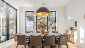Een moderne eetruimte met een ronde tafel, zes stoelen, een grote hanglamp en een potplant.