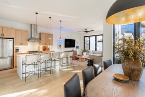A modern kitchen with wooden cabinets, a stainless steel refrigerator, and a dining area with a large table and chairs.