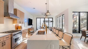 A modern kitchen with a central island, stainless steel appliances, and a large window providing natural light. - 6BDR Luxe Pool Retreat • City Views, Ping Pong, Foosball, Guest House | Henley (Austin)