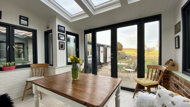 A dining area with a wooden table, chairs, and a view of the garden through large windows.