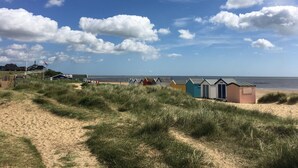 A beach with a row of colorful beach huts, a sandy path, and a clear blue sky with clouds.