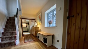 A staircase leading to a kitchen area with a wooden bench, a window with a flower arrangement, and a door.