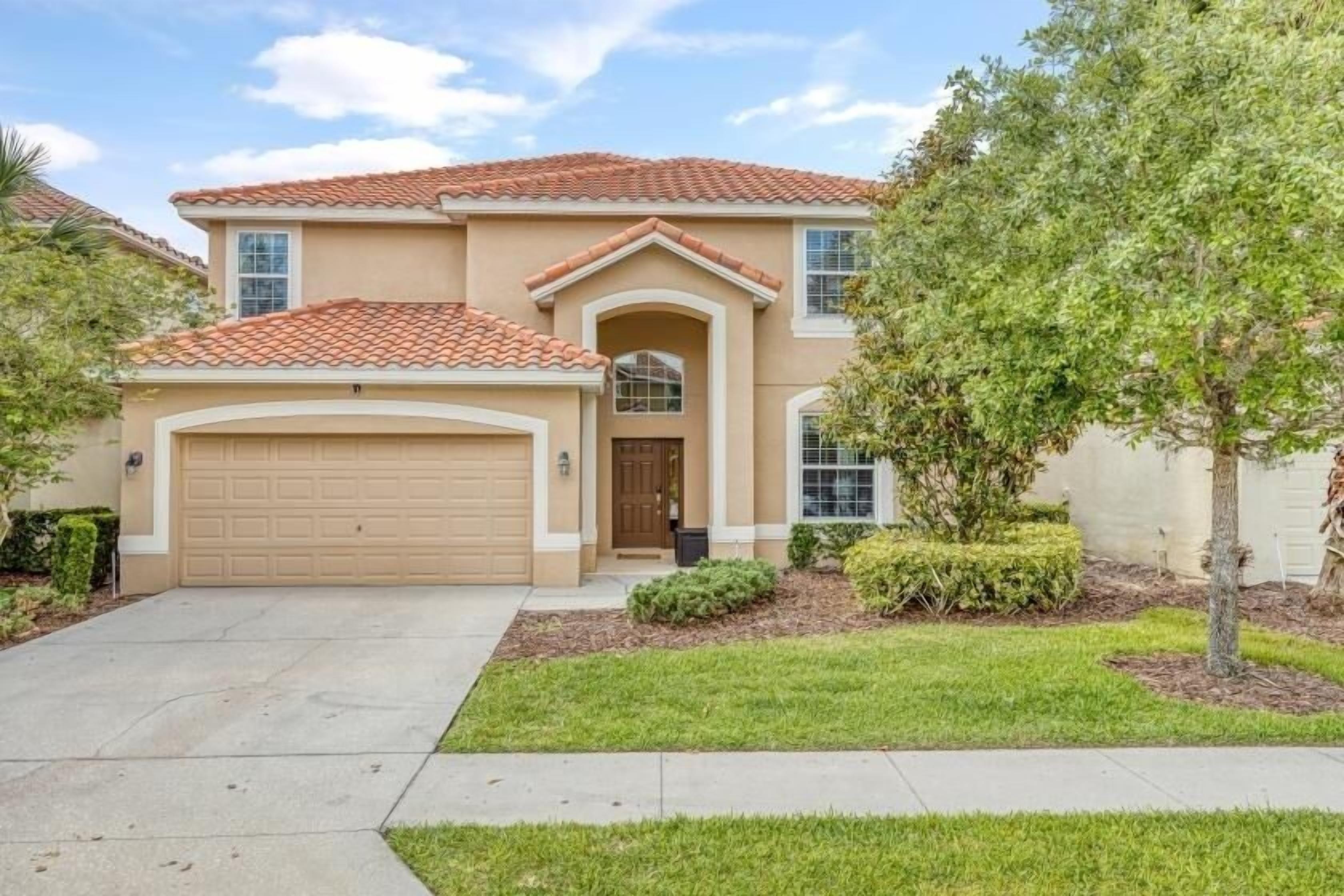 A two-story house with a beige facade, a red-tiled roof, and a front garage.