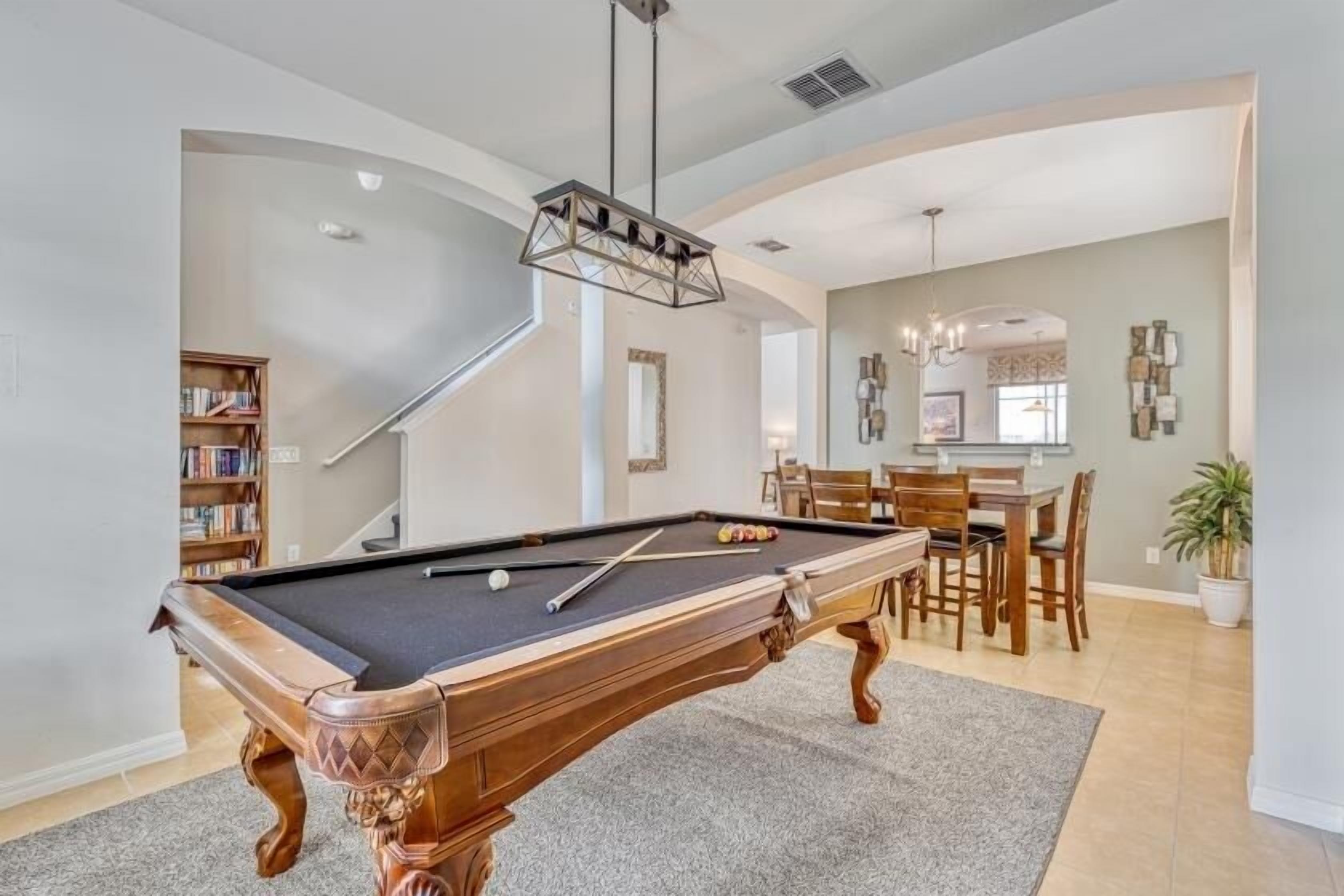 Une table de billard dans une pièce comprenant un escalier, un coin repas et une bibliothèque.