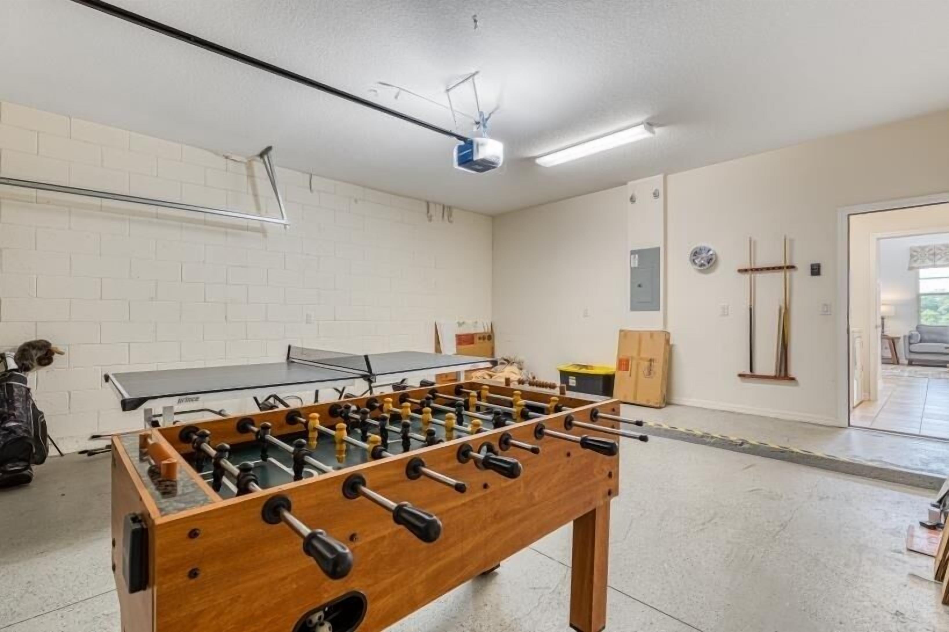 A room with a foosball table, a ping pong table, and a projector mounted on the ceiling.