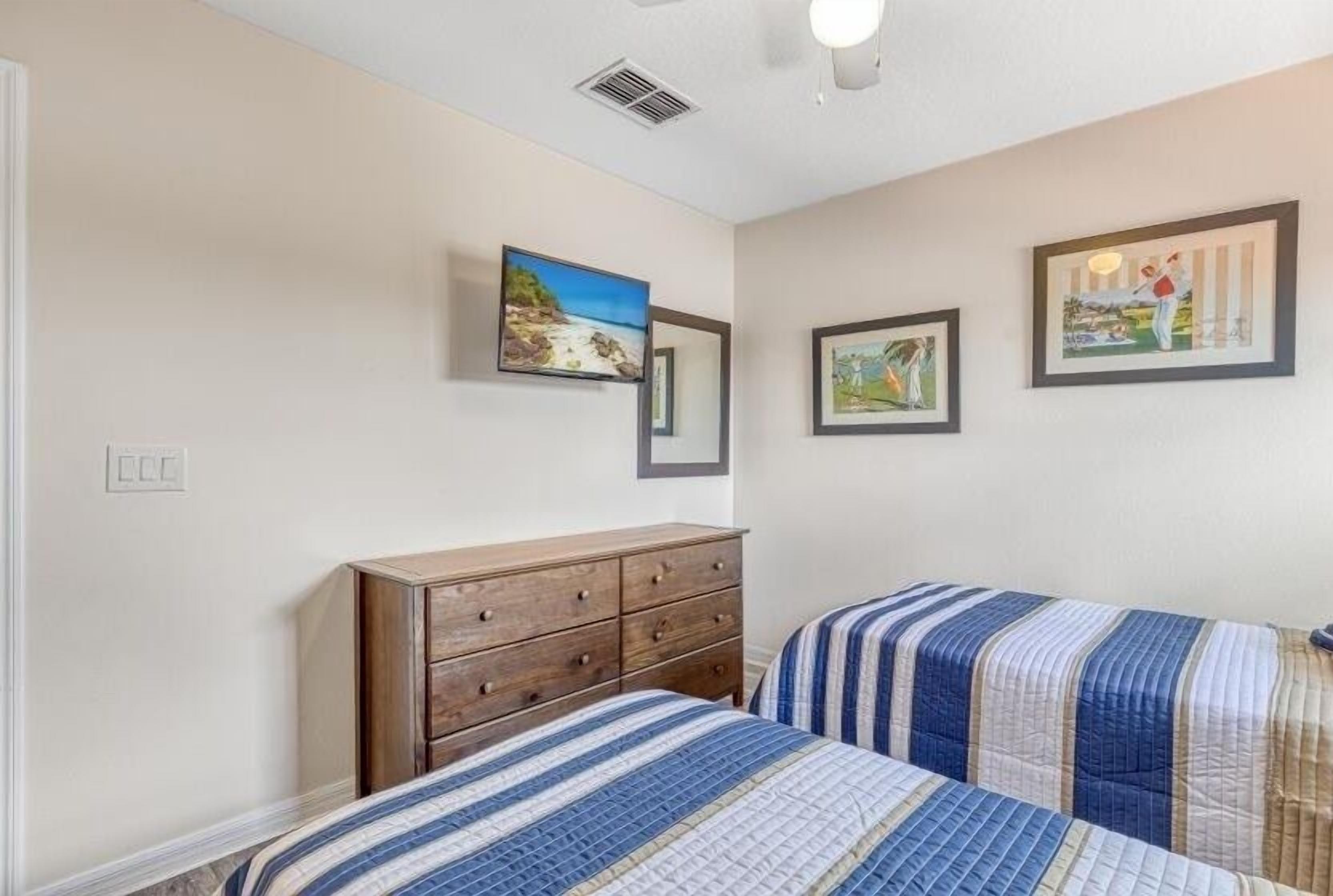 A bedroom with two beds, a wooden dresser, and three framed artworks on the wall.