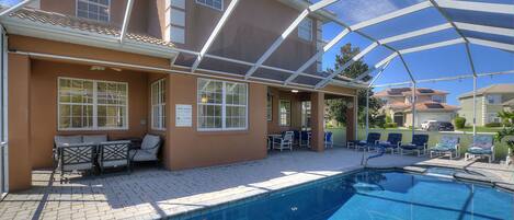 A swimming pool with a covered patio area, outdoor seating, and a clear blue sky.