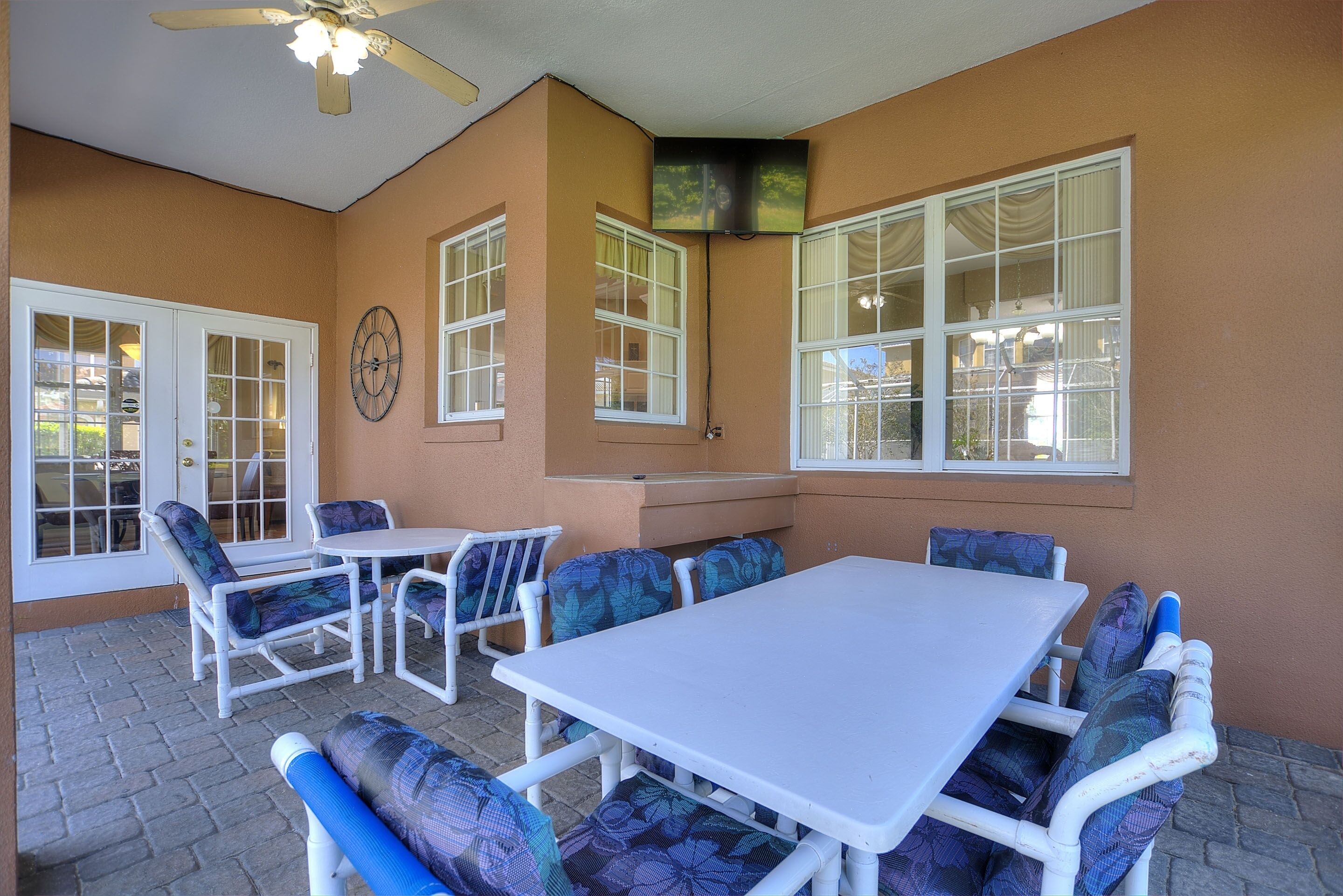 A patio area with a white table and chairs, a ceiling fan, and a television mounted on the wall.