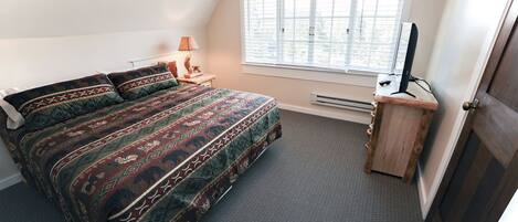 Un dormitorio con una cama grande, un escritorio con computadora, una ventana con persianas y una puerta.