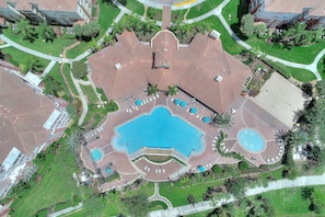 An aerial view of a hotel with a large central pool, multiple smaller pools, and a well-maintained garden area.