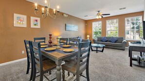 A dining area with a wooden table set for four, surrounded by chairs, a chandelier, and a ceiling fan. - Vista Cay Resort, Next To Universal 821 3 Bedroom Townhouse (Orlando)